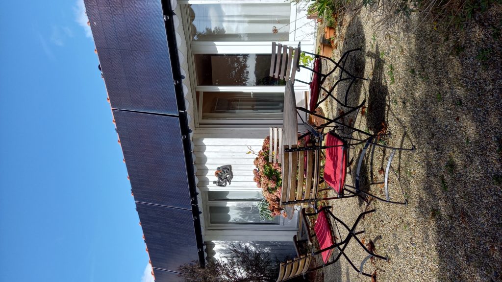 Terrasse avec un grande table et chaises devant le gîte avec vue sur le jardin